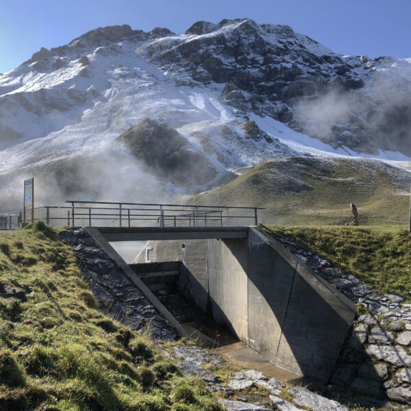 Brücke über den Cheselenbach (Melchsee) mit schneebedeckten Bergen im Hintergrund.