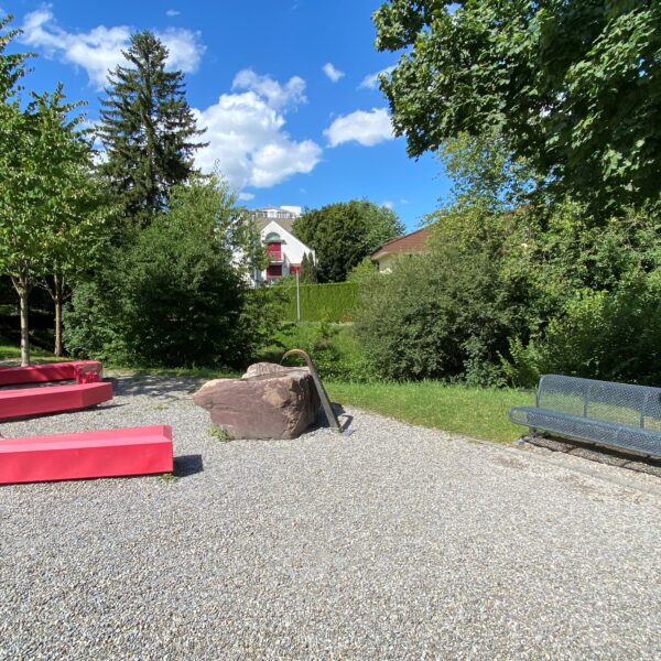 Chimlibach: Rote Bänke und eine Metallbank in einem Park unter blauem Himmel.