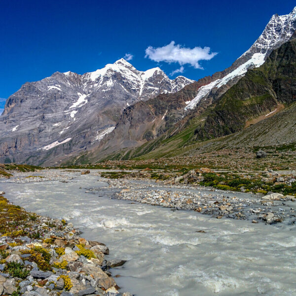 Berglandschaft mit dem Chrummbach im Vordergrund und schneebedeckten Gipfeln unter blauem Himmel.