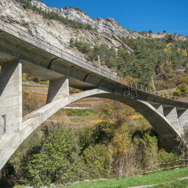 Betonbrücke in Drance, Schweiz, vor Bergkulisse und herbstlicher Vegetation.