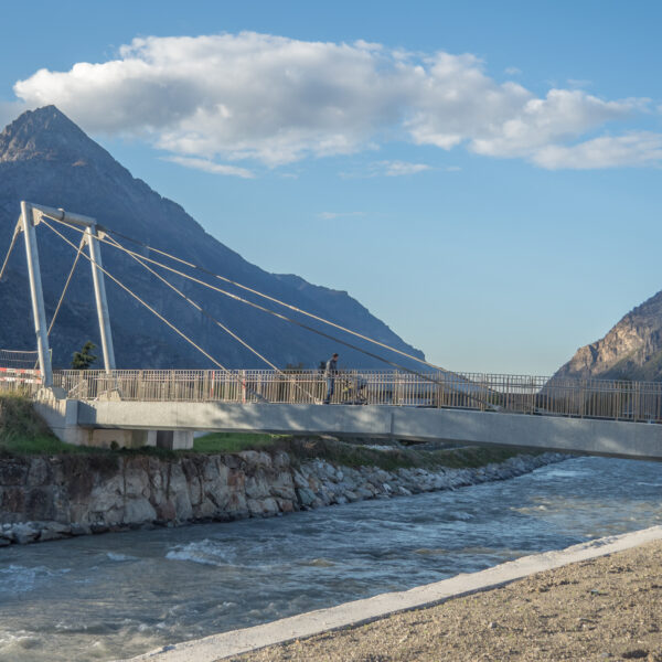 Fußgängerbrücke über die Drance mit Bergkulisse.