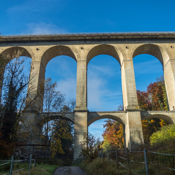 Glâne: Steinbogenbrücke mit Herbstlaub unter blauem Himmel.