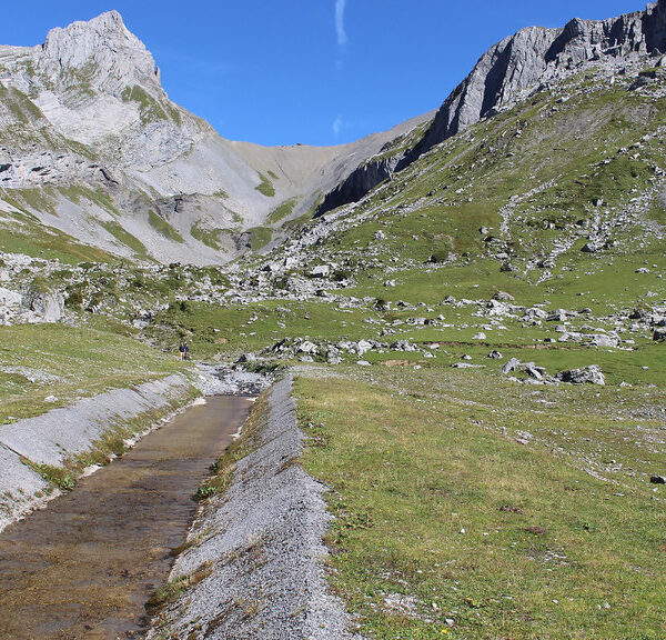 Glattalpseebach-Kanal vor alpiner Landschaft mit Bergen und grünen Wiesen.