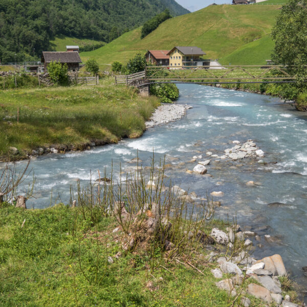 Fluss Hinter Schächen mit Brücke und Häusern vor grüner Hügellandschaft.