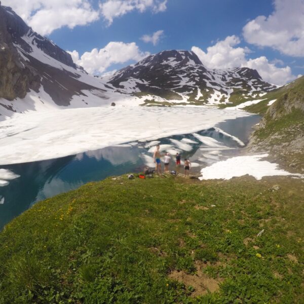 Iffigsee: Bergsee mit Eis, Schnee und Wanderern an einem sonnigen Tag.