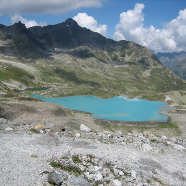 Türkisfarbener Jörisee in den Schweizer Alpen unter blauem Himmel mit Wolken.