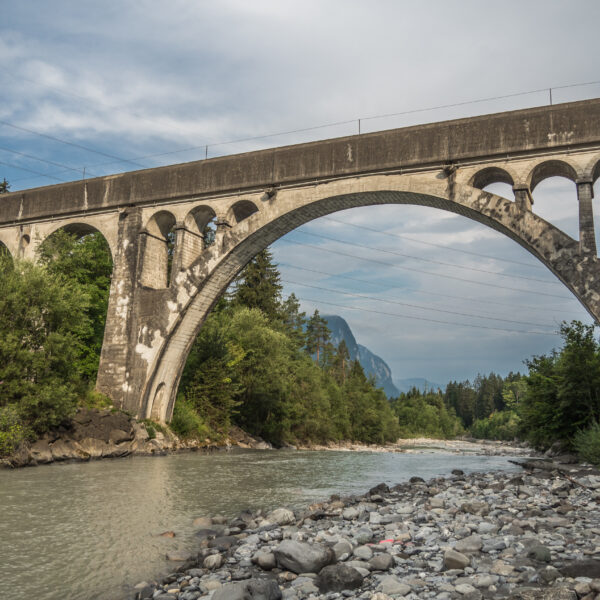 Kander: Steinbogenbrücke über Fluss in der Schweiz mit Bergen im Hintergrund.