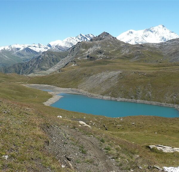 Türkisblauer Lac de Lona See in alpiner Landschaft mit schneebedeckten Bergen im Hintergrund.