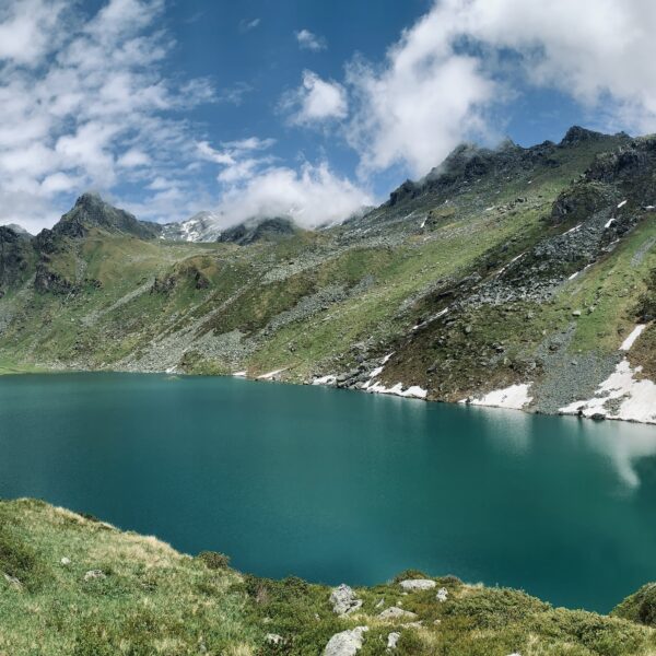 Lac de Louvie: Bergsee mit türkisfarbenem Wasser und grünen Hängen unter blauem Himmel.