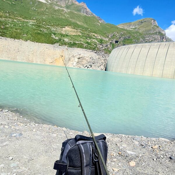 Lac de Moiry: Türkisblauer See mit Staumauer, Berglandschaft und Angelrute im Vordergrund.