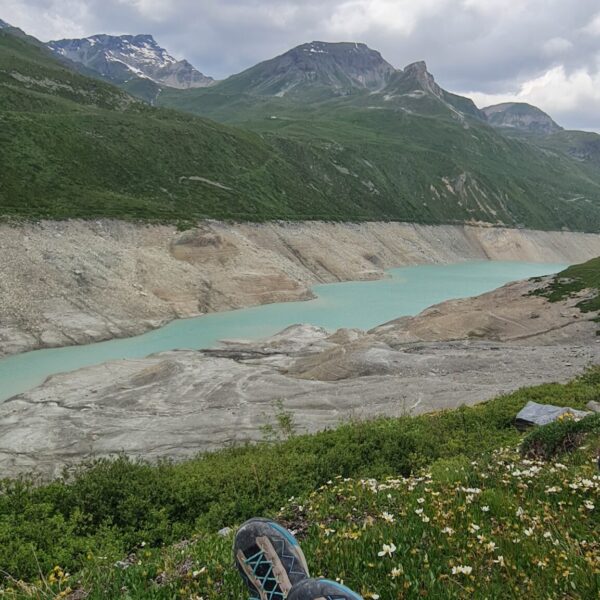 Füße mit Wanderschuhen vor dem Lac de Moiry in der Schweiz. Berglandschaft und blauer Himmel.