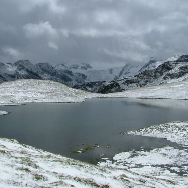 Lac des Autannes: Bergsee im Winter mit Schnee bedeckten Bergen unter bewölktem Himmel.
