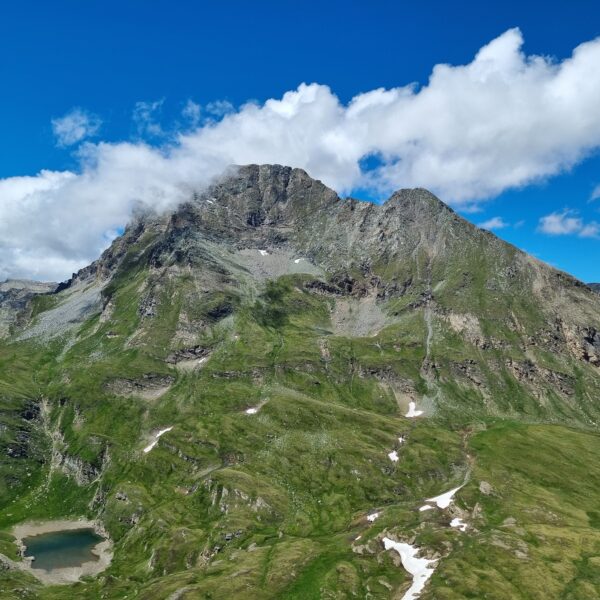 Lägh da Cam: Berglandschaft mit See und Wolken am blauen Himmel.