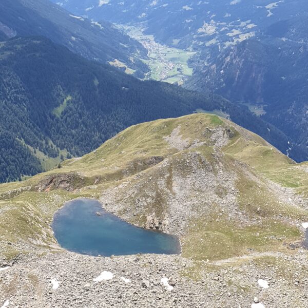 Lagh da Mürasciola: Bergsee in den Alpen mit grüner Umgebung und Tal im Hintergrund.