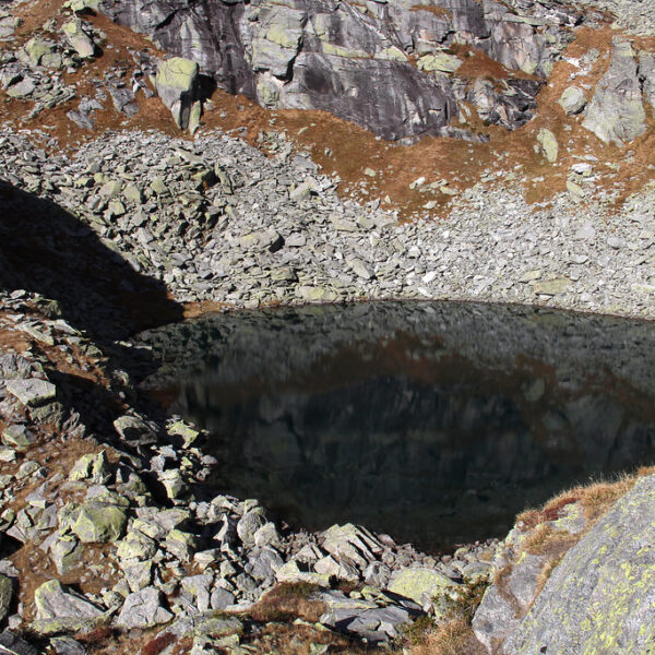 Lago Melo, ein Bergsee umgeben von Felsen und Geröll im Bosco. Reflexionen im Wasser.