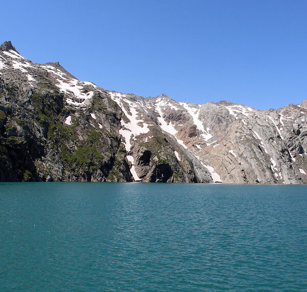 Lago dei Cavagnöö mit Bergen und Schnee unter blauem Himmel.