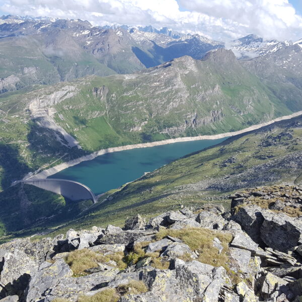 Lago di Lei Stausee mit Staumauer, umgeben von grünen Bergen und schneebedeckten Gipfeln.