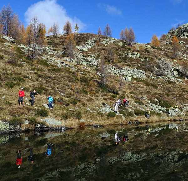 Wanderer am Lago di Mognola spiegeln sich im ruhigen Wasser des Bergsees.