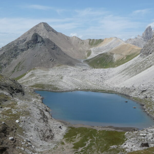 Lai Grond Bergsee in Surses, Graubünden mit felsiger Landschaft und blauem Himmel.