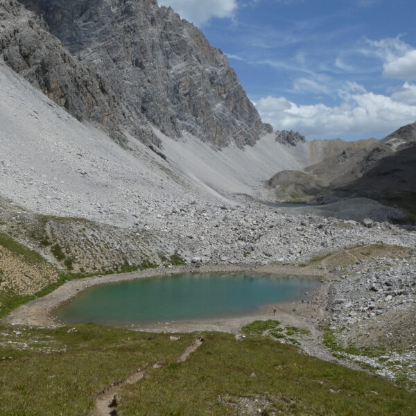 Lai Mort: Bergsee in alpiner Landschaft mit Geröllhalden und blauem Himmel.