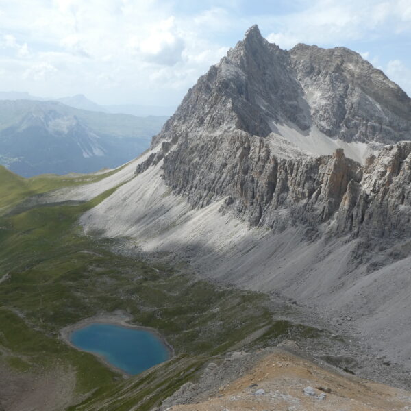 Lai Tigiel: Blauer Bergsee unterhalb eines schroffen Berggipfels in Graubünden, Schweiz.