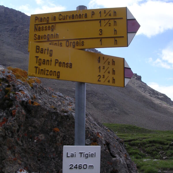 Gelbes Wanderschild am Lai Tigiel, Schweiz, mit Wegweisern nach Plang la Curvanera, Nassegl, Savognin, Bartg, Tinizong. 2460m Höhe.
