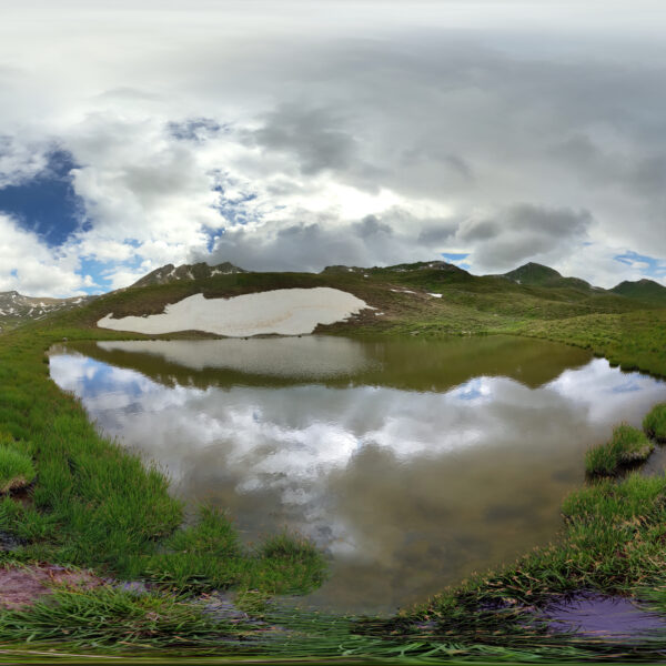 Lai da Schmorras: Bergsee mit Spiegelung der Wolken und grüner Landschaft in Graubünden, Schweiz.