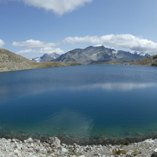 Lej da la Tscheppa: Bergsee in Graubünden, umgeben von felsiger Landschaft unter blauem Himmel.