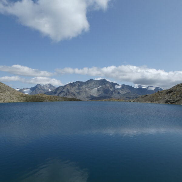 Lej da la Tscheppa: Ruhiger Bergsee mit Spiegelung der umliegenden Alpen und Wolken.