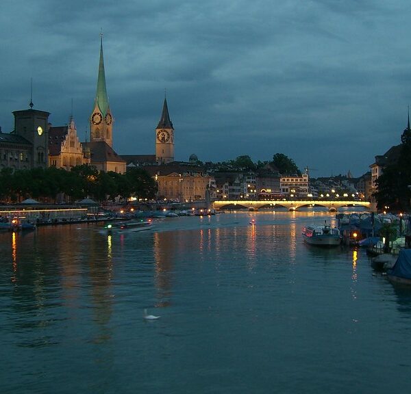 Limmat Fluss Zürich bei Nacht mit beleuchteten Gebäuden und Brücke.