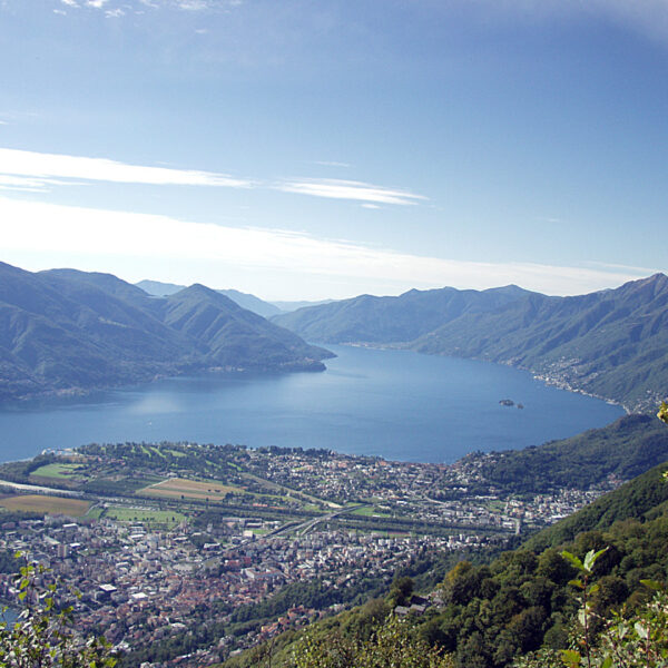 Blick auf Maggia und den Lago Maggiore, umrahmt von Bergen unter blauem Himmel.
