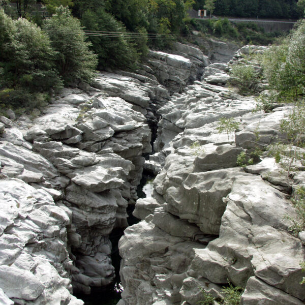Grauer Felsenschlucht im Maggiatal mit Wasserlauf und Bäumen.