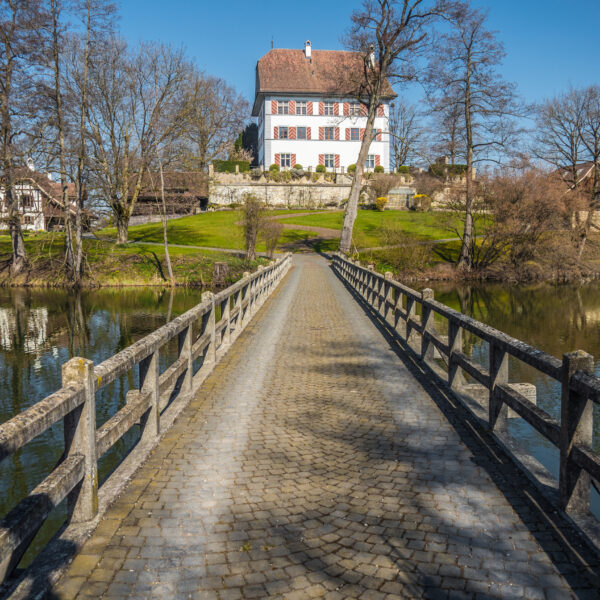 Brücke zum Schloss Mauensee, Schweiz. Historisches Gebäude mit roten Fensterläden.