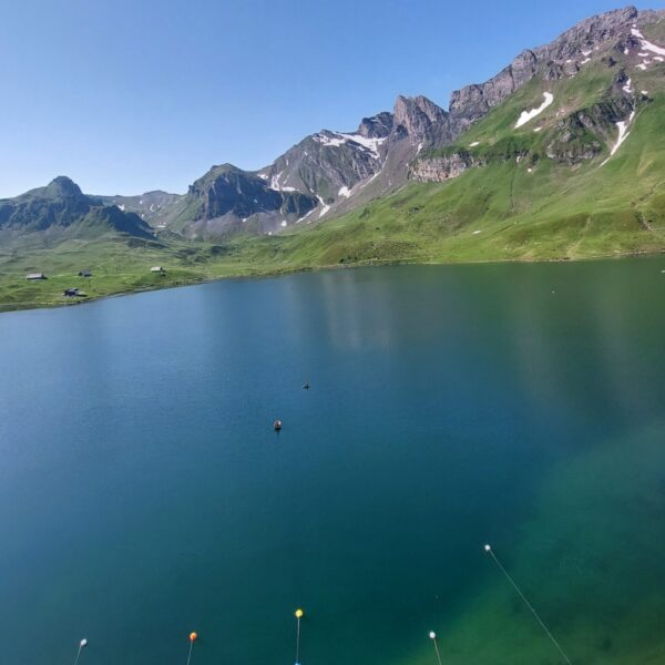 Melchsee: Blauer Bergsee mit grünen Wiesen und schneebedeckten Gipfeln im Hintergrund.