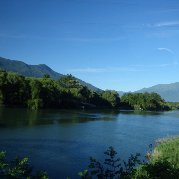 Flusslandschaft mit Bergen und üppigem Grün unter blauem Himmel