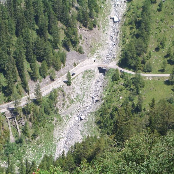 Berglandschaft mit Flussbett, Brücke und Straße, umgeben von grünen Bäumen.