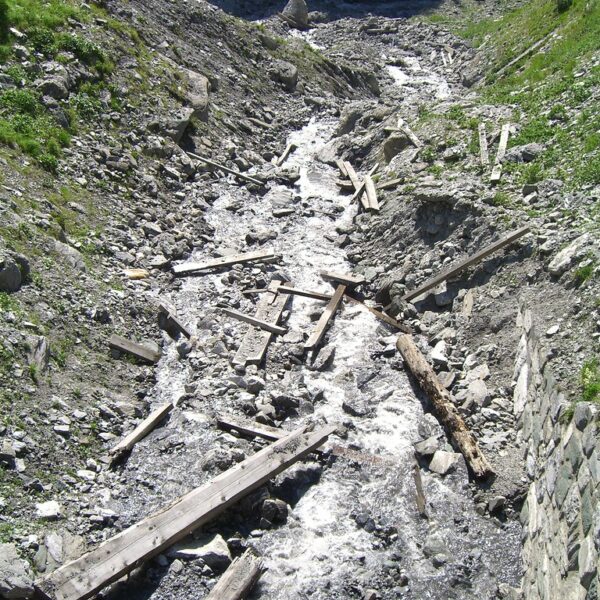Geröllhalde mit Bachlauf und Holzresten. Natürliche Landschaft.