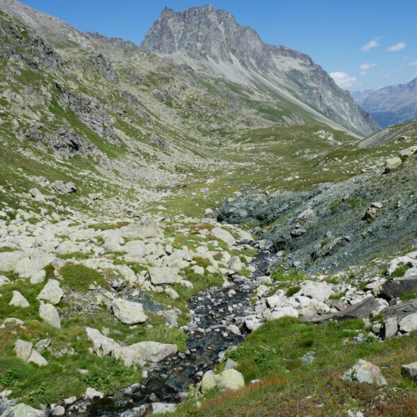 Ova dal Mulin: Berglandschaft mit Bachlauf und Felsen unter blauem Himmel.