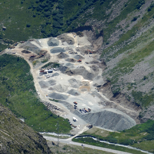 Ova dal Vallun: Luftaufnahme von einer Baustelle in den Bergen mit Schotterhaufen und Baufahrzeugen.