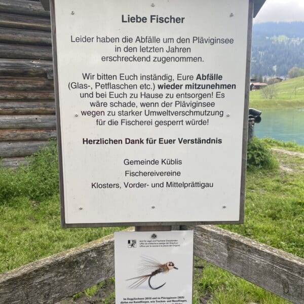 Ein Schild auf Deutsch bittet Fischer, ihren Müll zum Schutz des Plävigginersees wieder mitzunehmen. Es weist auf die zunehmende Müllmenge hin und dankt für ihr Verständnis. Unter dem Hauptschild ist ein kleiner Flyer mit einer Fischillustration angebracht.