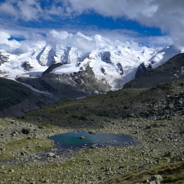 Puoz Bass: Bergsee in hochalpiner Landschaft mit schneebedeckten Gipfeln und Wolken
