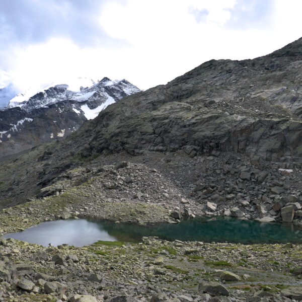 Bergsee Puoz Ot mit schneebedeckten Gipfeln im Hintergrund.