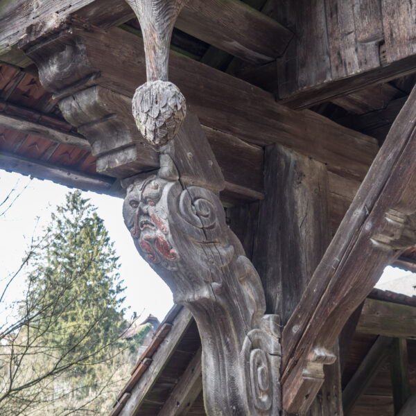 Holzgeschnitzte Figur am Rotbach (Rothenburg) mit Gesicht und Ornamenten.