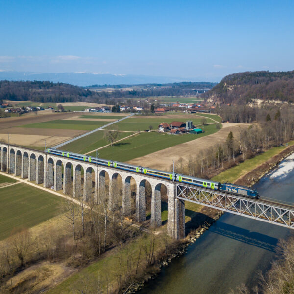 Zug überquert die Saane auf einem Viadukt in grüner Landschaft.