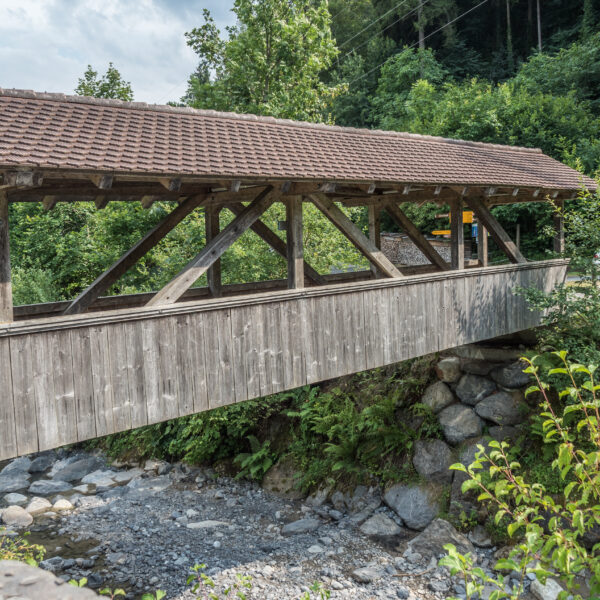 Gedeckte Holzbrücke über den Saxetbach, umgeben von üppigem Grün.