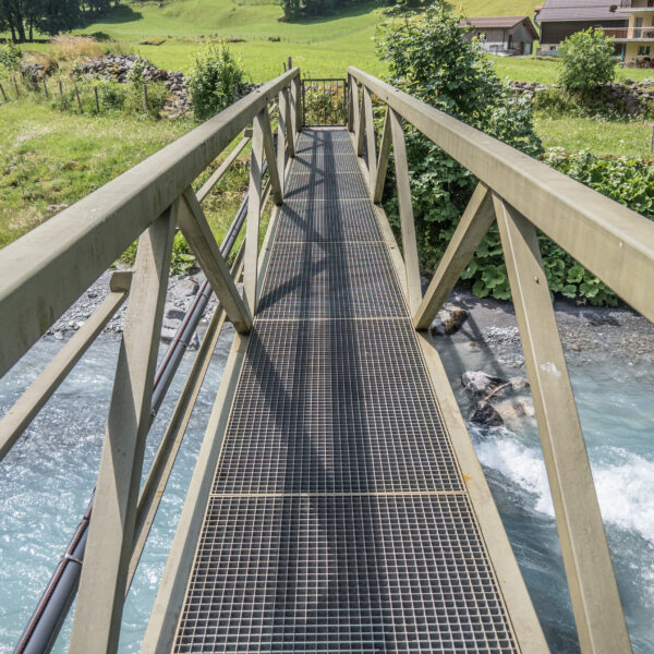 Metallbrücke über türkisfarbenen Fluss in Schächen. Landschaft mit grünen Wiesen.