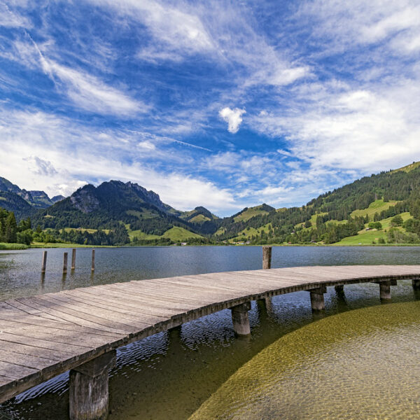 Holzsteg am Schwarzsee mit Bergen und blauem Himmel.