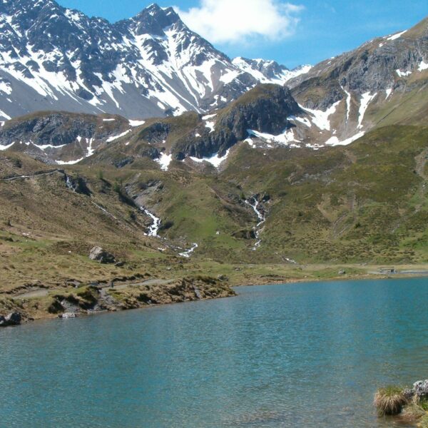 Schwellisee: Bergsee mit schneebedeckten Gipfeln und blauem Himmel.