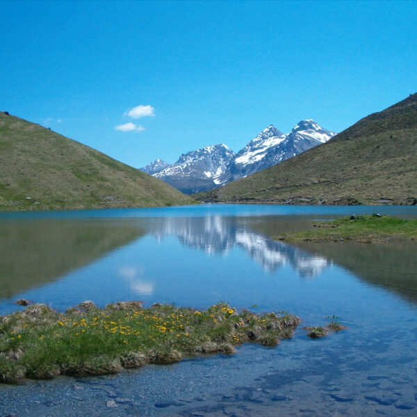 Schwellisee: Bergsee mit Spiegelung der schneebedeckten Gipfel und blauem Himmel.
