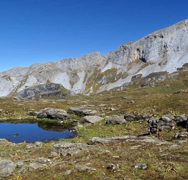 Seelenen: Bergsee in alpiner Landschaft mit markantem Felsmassiv unter blauem Himmel.